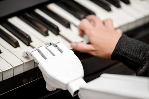 A robotic hand and a human hand play a piano keyboard together