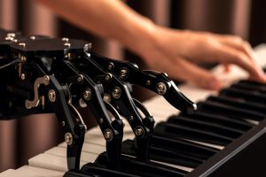 A robotic hand plays a piano while a human hand hovers above