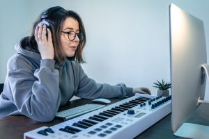 Person wearing headphones sits at a desk with a computer and music keyboard