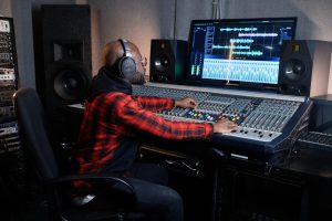 Person in a red plaid shirt adjusts audio controls at a sound mixing console