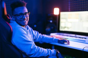 Person with glasses smiles while sitting at a computer in a music studio