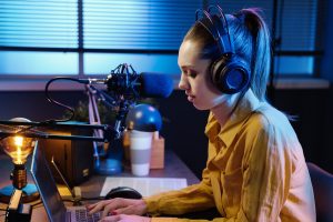 A person in headphones sits at a desk with a laptop and microphone, focused on work