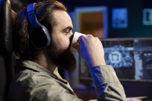 Person wearing headphones drinking from a cup while seated at a computer